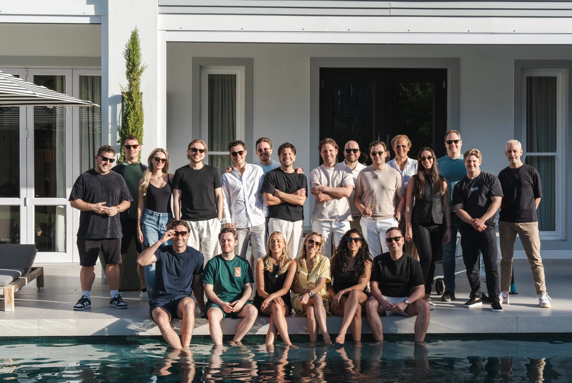 De founders en builders van Deel I samen bij de villa in Kaapstad, sommigen staand, anderen zittend aan de rand van het zwembad.