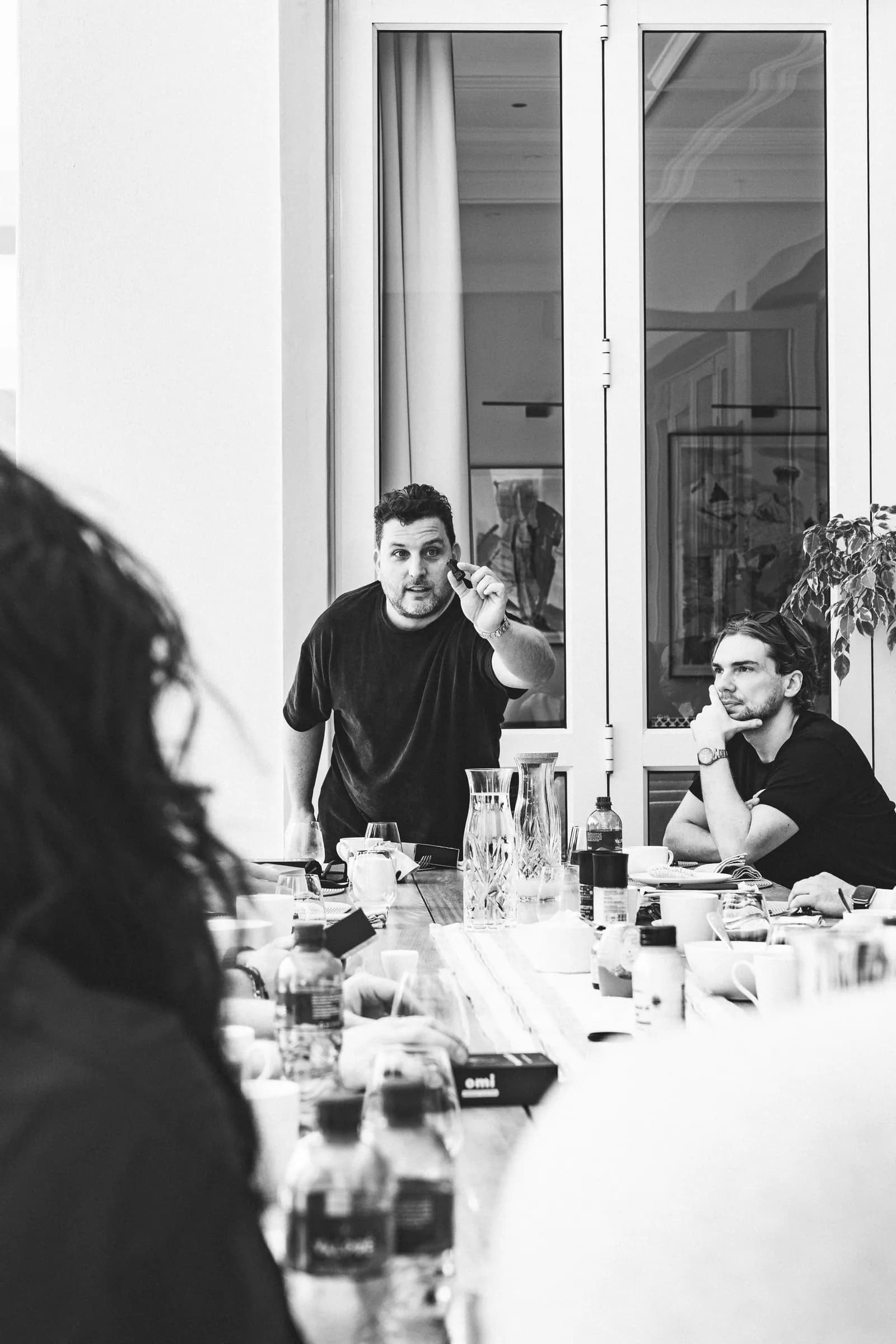 Zwart-witfoto: een founder is aan het woord aan de lange tafel in de villa, terwijl de anderen luisteren.